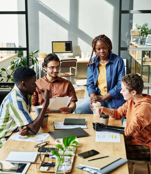 Group of young employees gathered by table in office to have coffee and discuss some working points concerning new business project